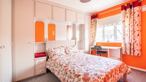 A bedroom with a bed, a desk, and a chair. There is a window with curtains.