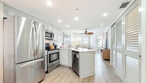 A modern kitchen with stainless steel appliances, white cabinetry, and a wooden floor. - Beach Luxury Resort | Bay Views (St. Pete Beach)