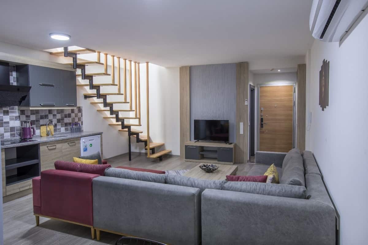 A modern living room with a grey sofa, a TV, and a wooden staircase.