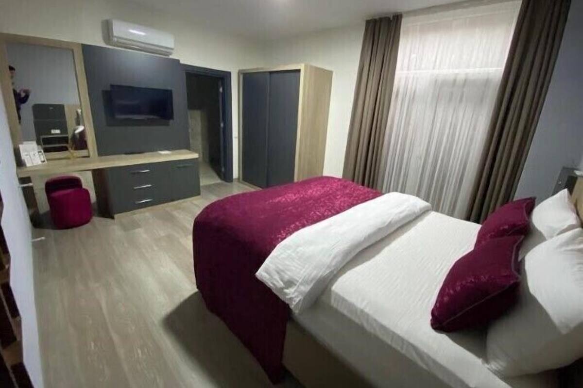 A modern hotel room with a bed, a desk, a TV, and a wardrobe.
