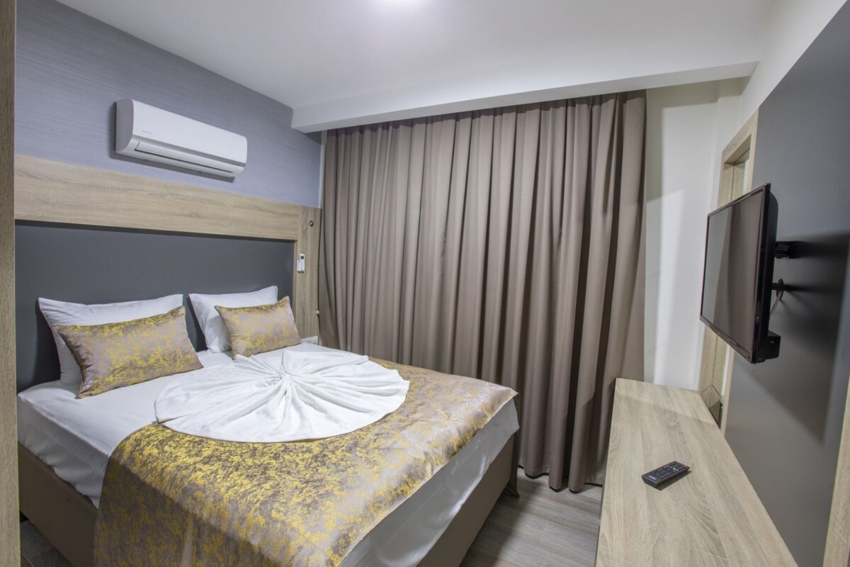 A hotel room with a bed, a TV, an air conditioner, and a curtain.
