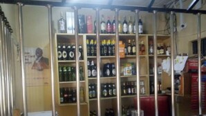 A bar with shelves stocked with various bottles, a counter with a menu, and a mirror reflecting the interior. - Senior Chief Wambugu Palace (Marua)