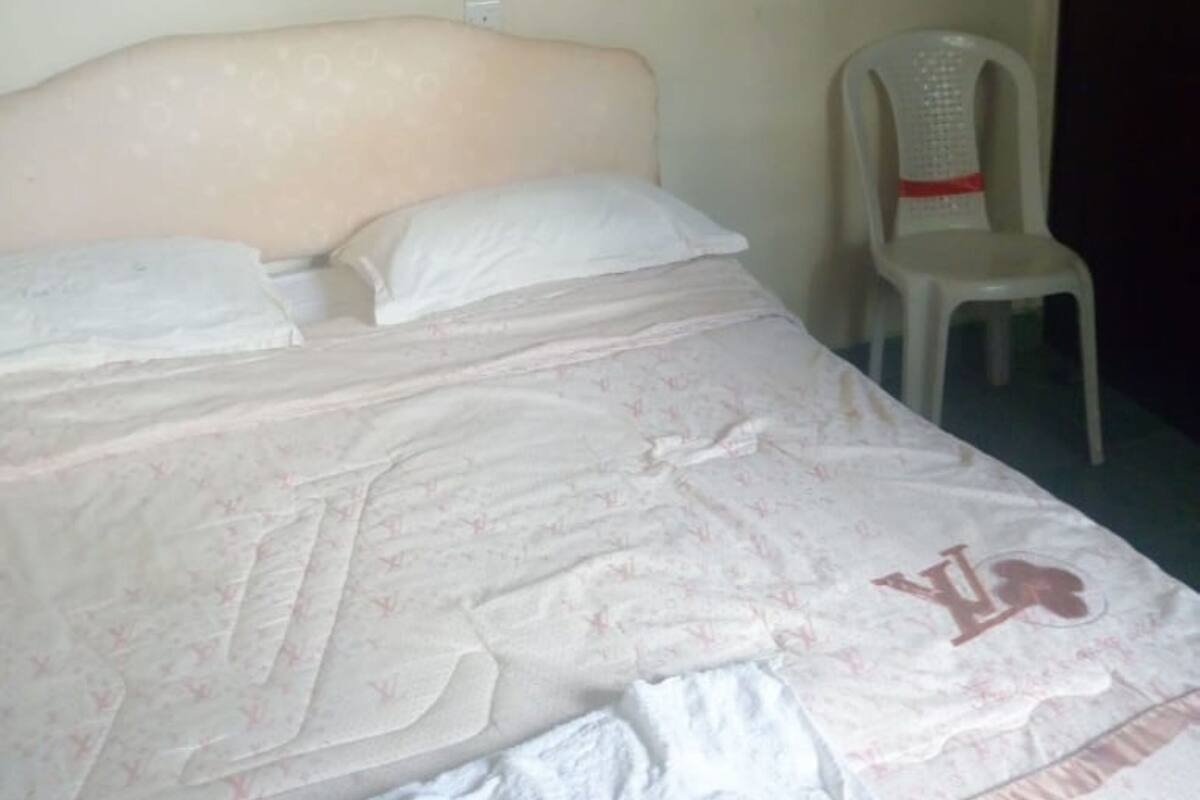 A bed with a patterned bedspread, a white pillow, and a chair with a red trim.