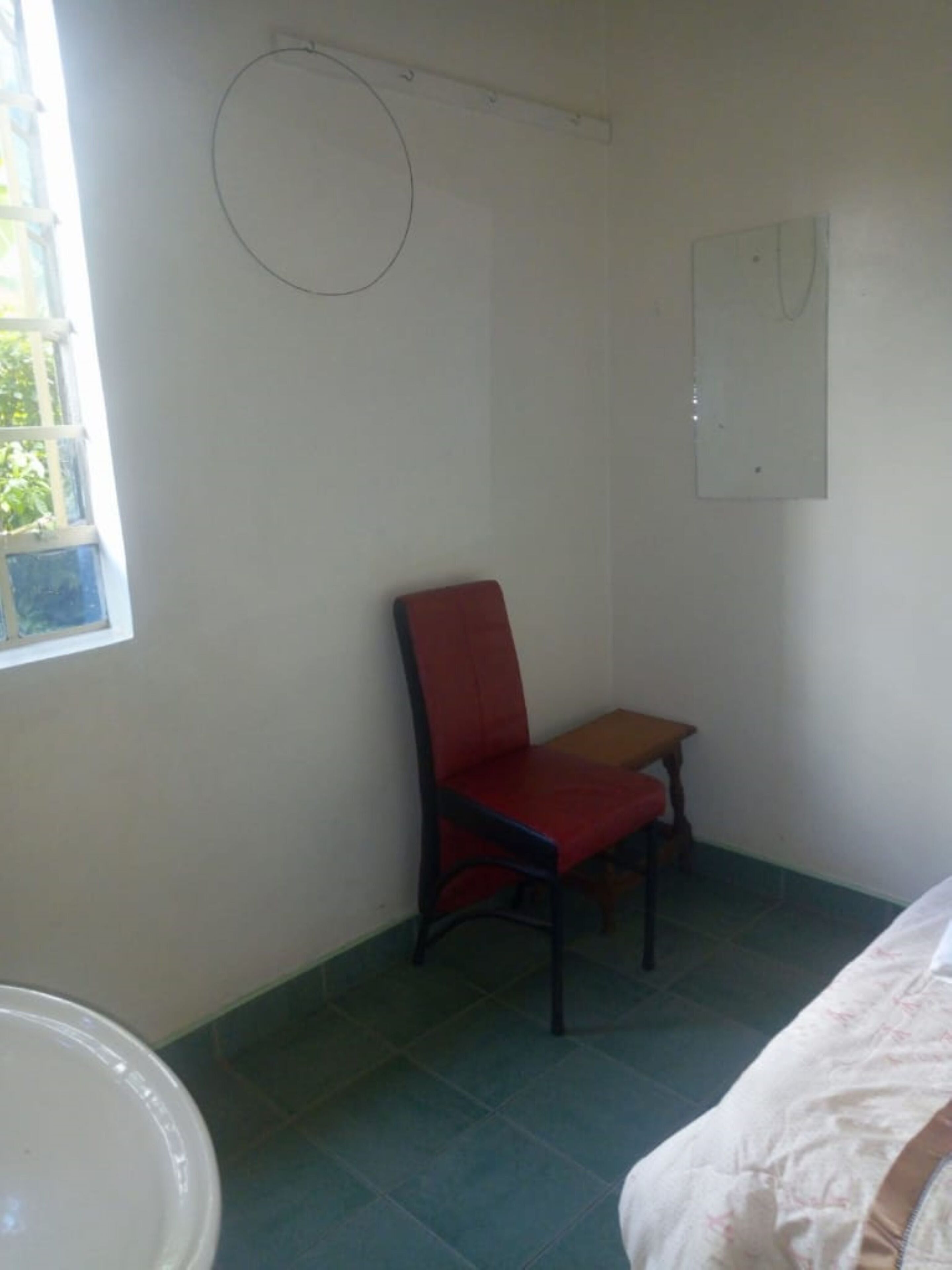 Una habitación con una cama, una silla roja, una mesita y una ventana.