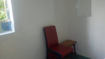 Una habitación con una cama, una silla roja, una mesita y una ventana.