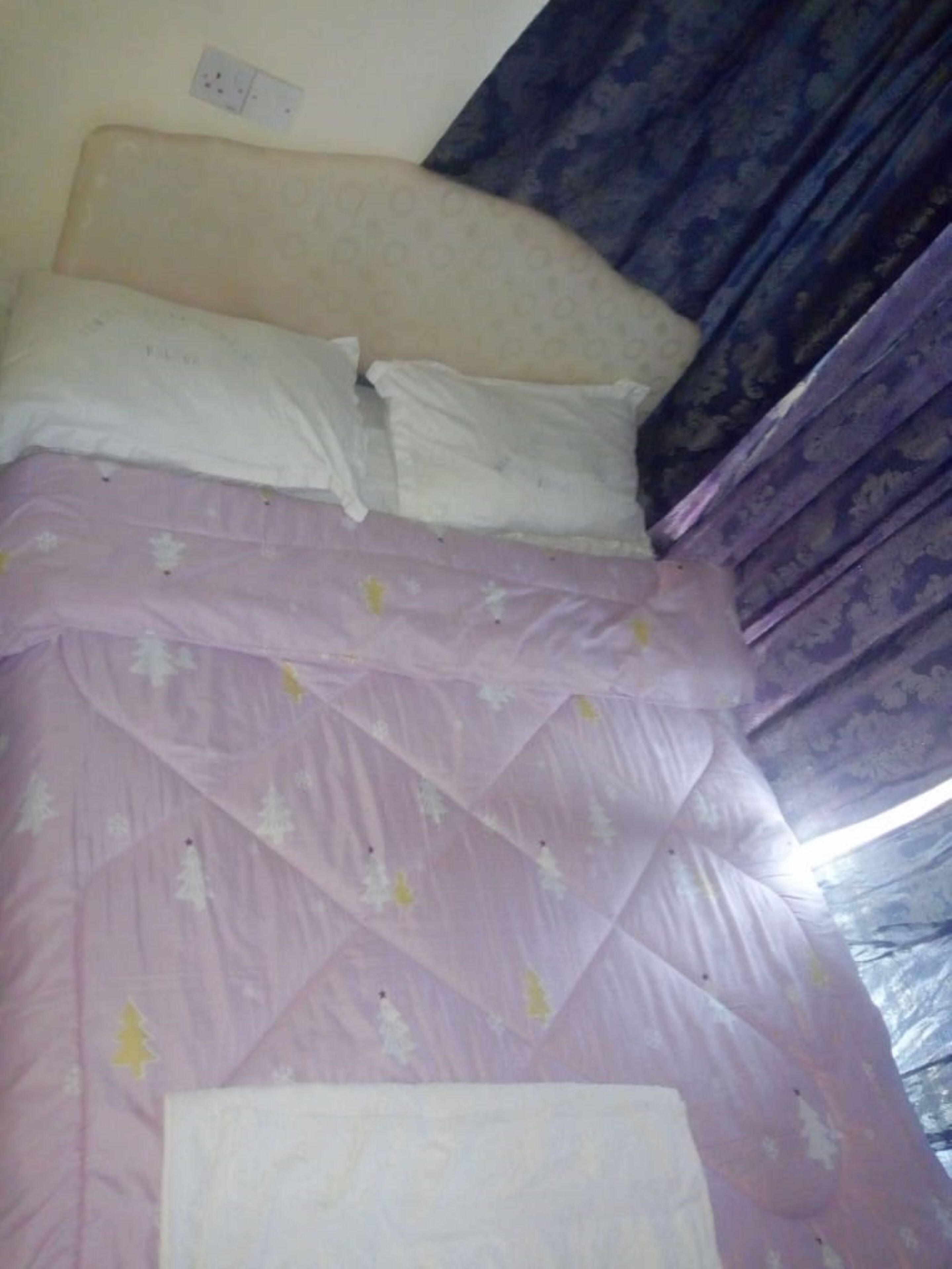 A bed with a headboard, white pillows, and a purple bedspread with tree patterns.