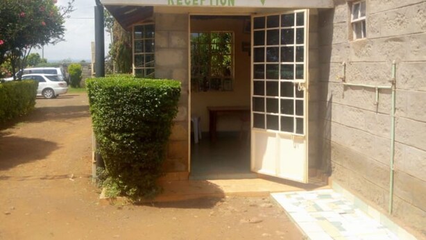 A reception area with a sign above the door, a small covered entrance, and a dirt path leading to it. - Senior Chief Wambugu Palace (Marua)