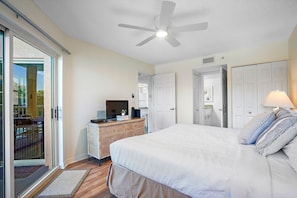 A bedroom with a bed, a ceiling fan, a television on a dresser, and a door leading to another room.