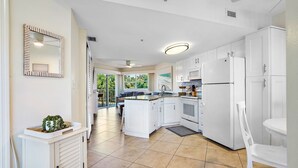 Eine moderne Küche mit weißen Schränken, einem eingebauten Backofen und einem Kühlschrank. Ein Essbereich mit Tisch und Stühlen ist ebenfalls vorhanden.