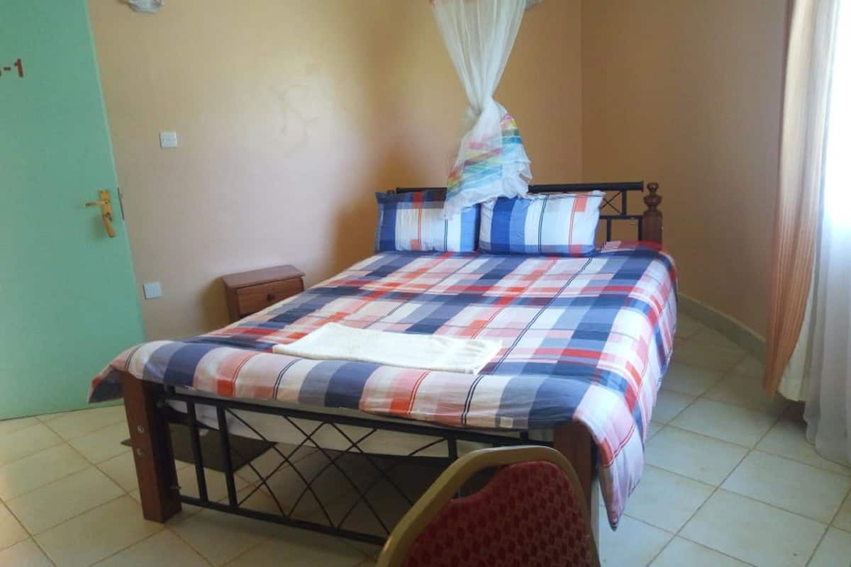 Un dormitorio con una cama, una mesita de noche, una silla y un mosquitero sobre la cama.