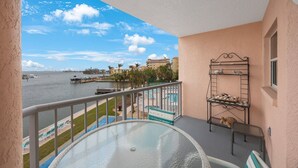 A balcony with a view of a marina, a pool, and a building across the water. - Coastal Getaway | Resort Amenities (St. Pete Beach)