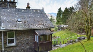 A stone house with a sloped roof, a small attached wooden structure, and a garden with a pathway and a tree. - Squirrel’s Retreat - UK30821 (Thornthwaite, near Keswick)