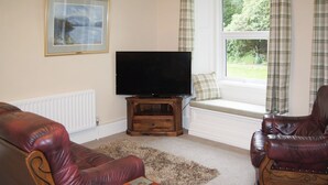 A living room with a television, two leather sofas, a wooden coffee table, and a window with curtains. - Squirrel’s Retreat - UK30821 (Thornthwaite, near Keswick)