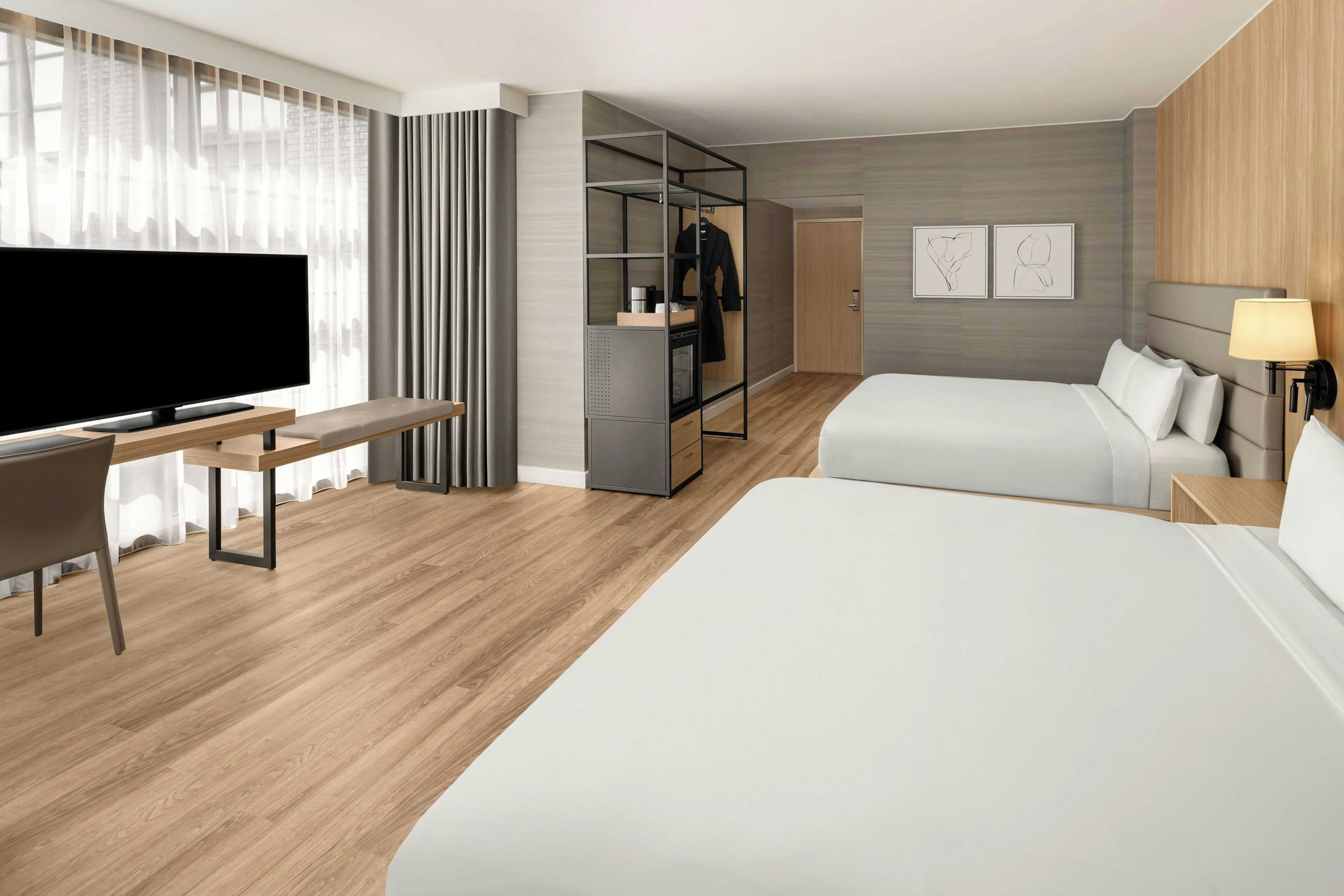 A hotel room with a bed, a desk with a TV, a wardrobe, and a bedside lamp.