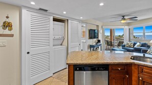 A kitchen with a built-in dishwasher, a dining area with a TV, and a view of the ocean. - Luxury Coastal Getaway | Resort Perks (St. Pete Beach)