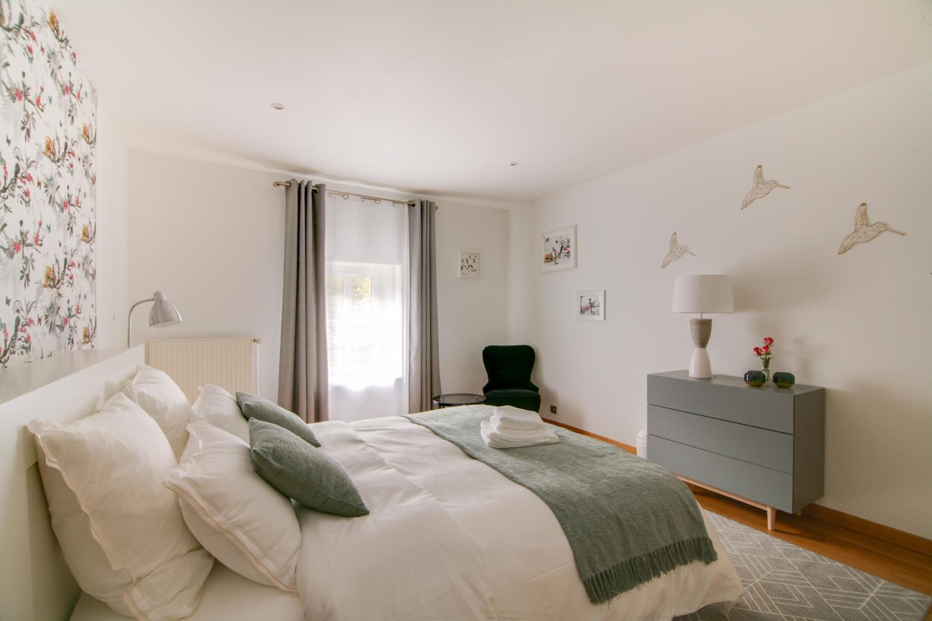 Un dormitorio con cama, cómoda, silla y ventana con cortinas.