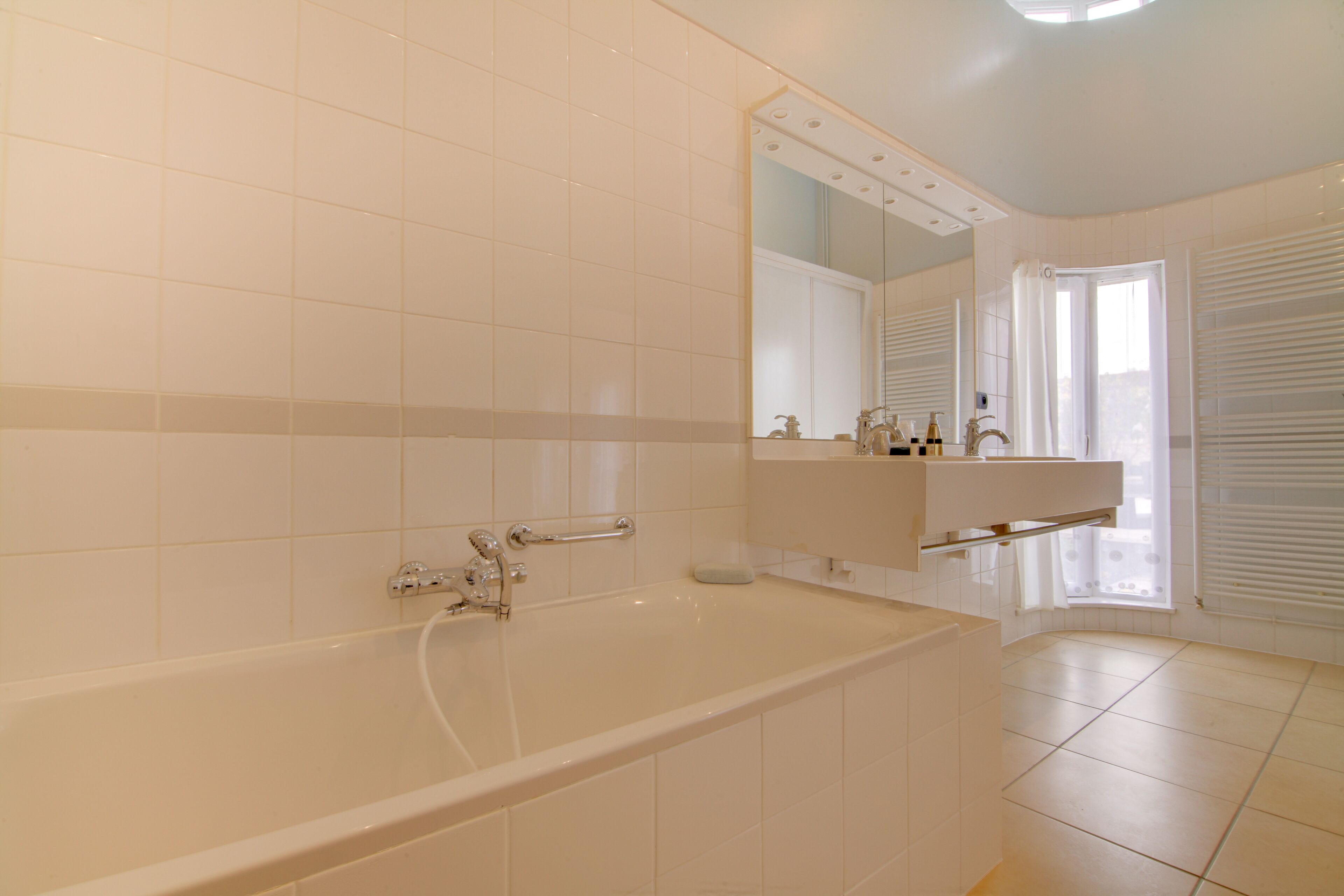 Ein modernes Badezimmer mit einer Badewanne, einem großen Spiegel und einem Fenster mit Jalousien.