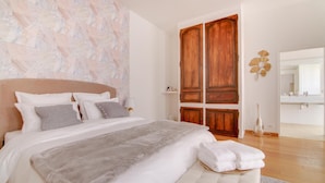 Un dormitorio con una cama grande, un armario de madera y un baño visible a través de una puerta abierta.