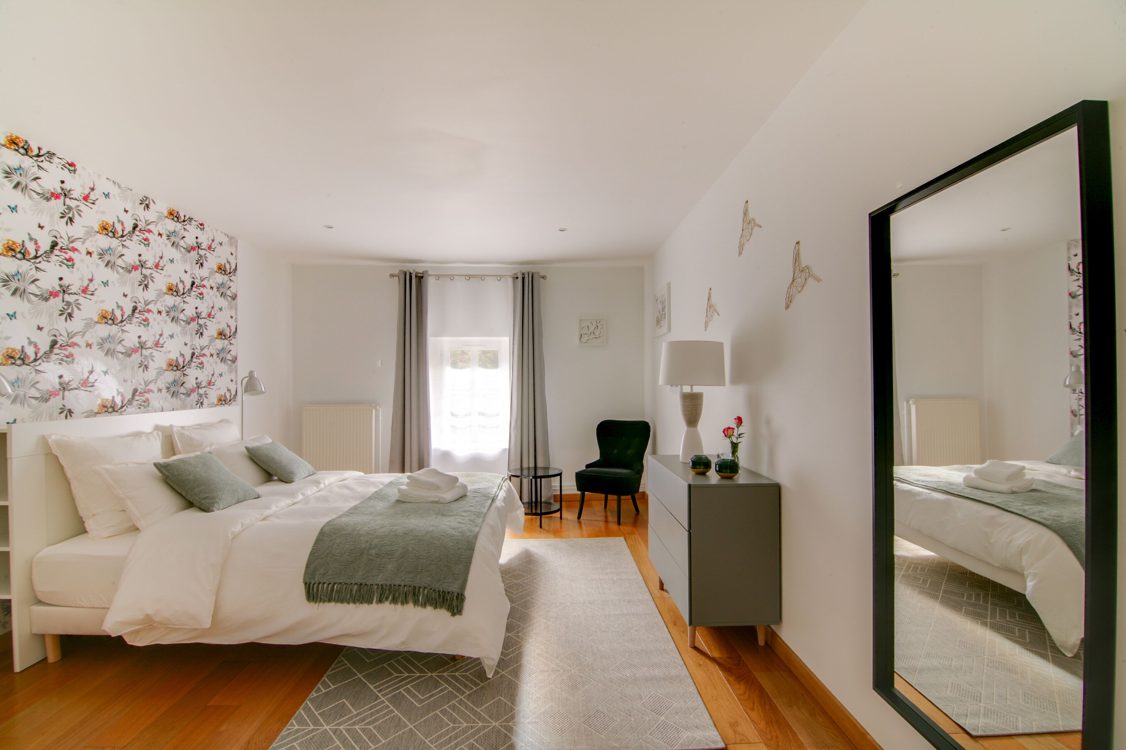 A bedroom with a bed, a chair, a dresser, and a mirror.