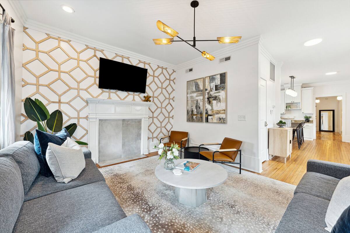 A modern living room with a fireplace, a flat-screen TV mounted on the wall, and a dining area in the background.