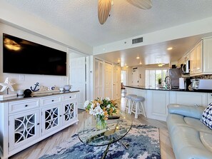A modern kitchen with white cabinetry, a large island, and a flat-screen TV mounted above the counter.