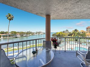 A balcony with a glass table, chairs, a flower vase, and a view of a marina and buildings.