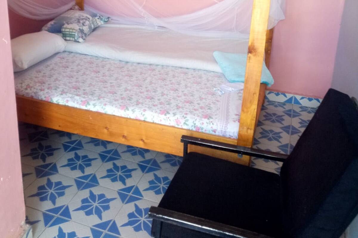 A small, single-bed room with a wooden frame, a mosquito net, and a floral bedspread.
