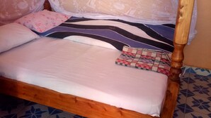 Ein hölzernes Bett mit Baldachin, gemusterten Kissen und einer karierten Decke.