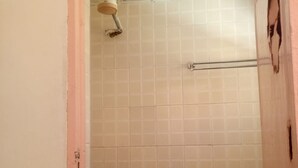 Ein Badezimmer mit Duschbereich in weißen Fliesen, einer sichtbaren Rohrleitung und einer Toilette.
