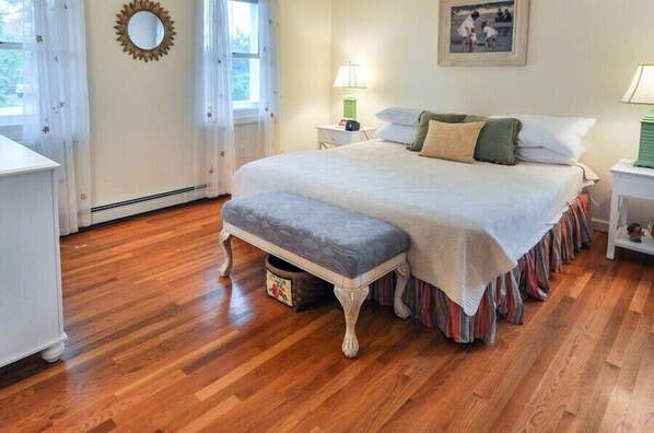 A bedroom with a large bed, a bedside table, a lamp, and a window with curtains.