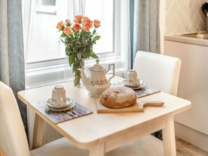 A table with a teapot, cups, a loaf of bread, and a vase of flowers.