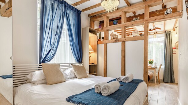Une chambre à coucher avec un lit, un rideau bleu, un lustre et une structure de plafond en bois.
