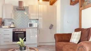 Une cuisine moderne équipée d’un four à micro-ondes, d’un four et d’une bouilloire, une table ronde en verre agrémentée d’une plante, et un canapé marron avec un coussin à carreaux.