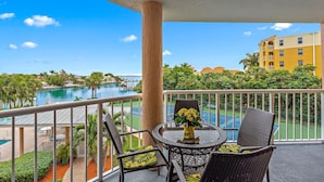A balcony with wicker furniture, a glass table, and a vase of flowers.