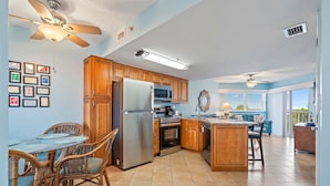 A kitchen with wooden cabinets, a stainless steel refrigerator, a microwave, and a dining area with wicker chairs and a glass table.