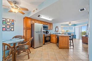A kitchen with wooden cabinets, a stainless steel refrigerator, a microwave, and a dining area with wicker chairs and a glass table.