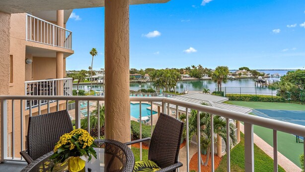 A balcony with wicker chairs and a table, overlooking a pool and a marina with boats.