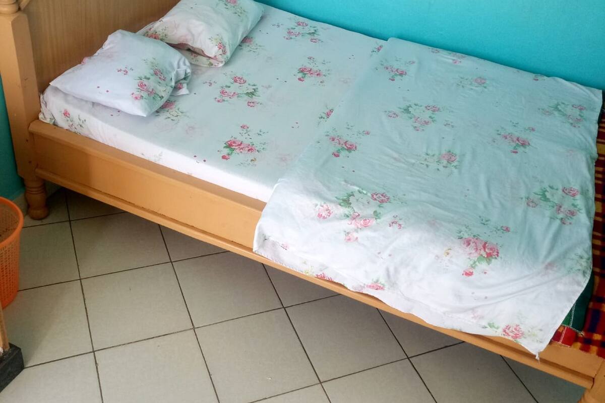 A single bed with floral bedding in a room with tiled flooring and a wooden headboard.