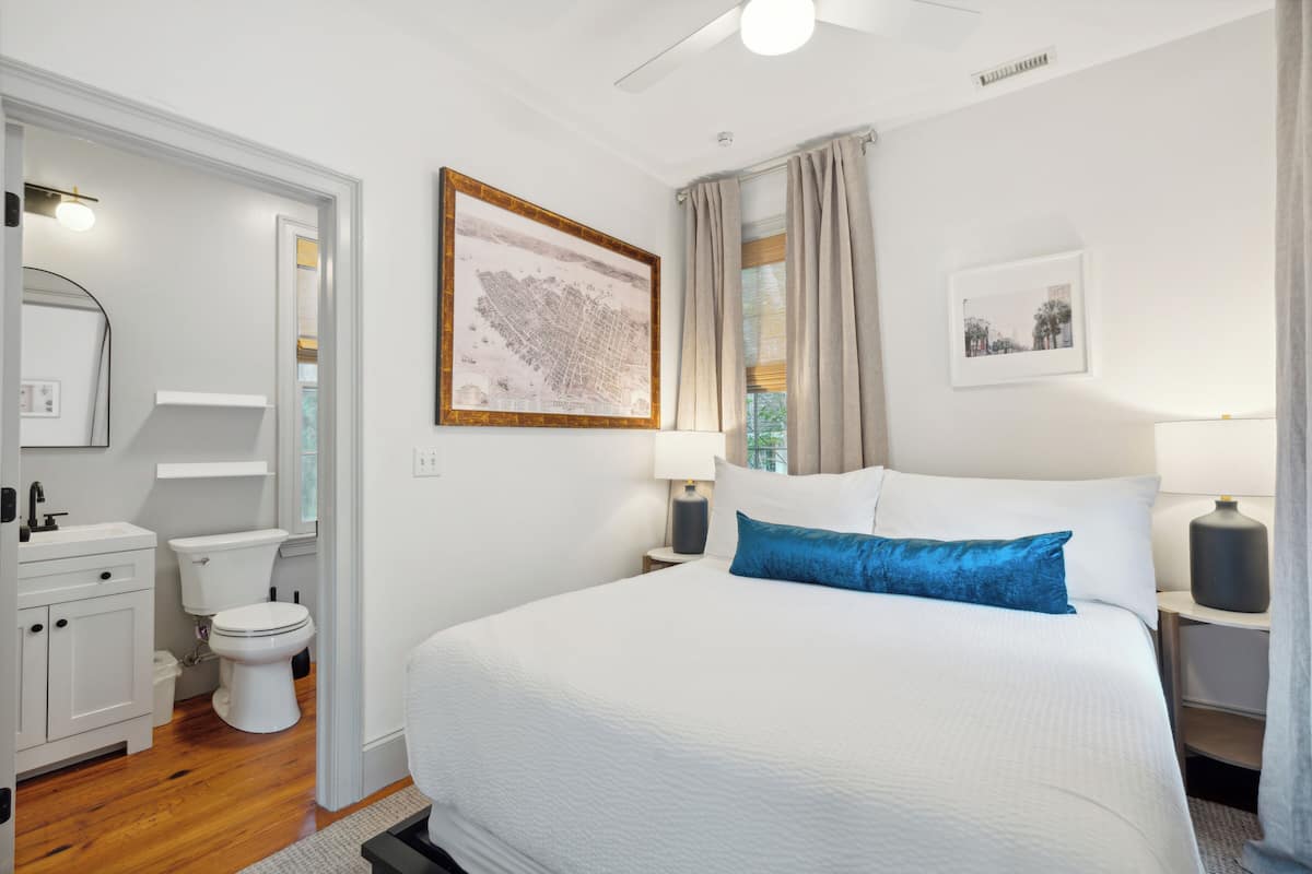 A hotel room with a large bed, a white bathroom, and a cityscape painting on the wall.