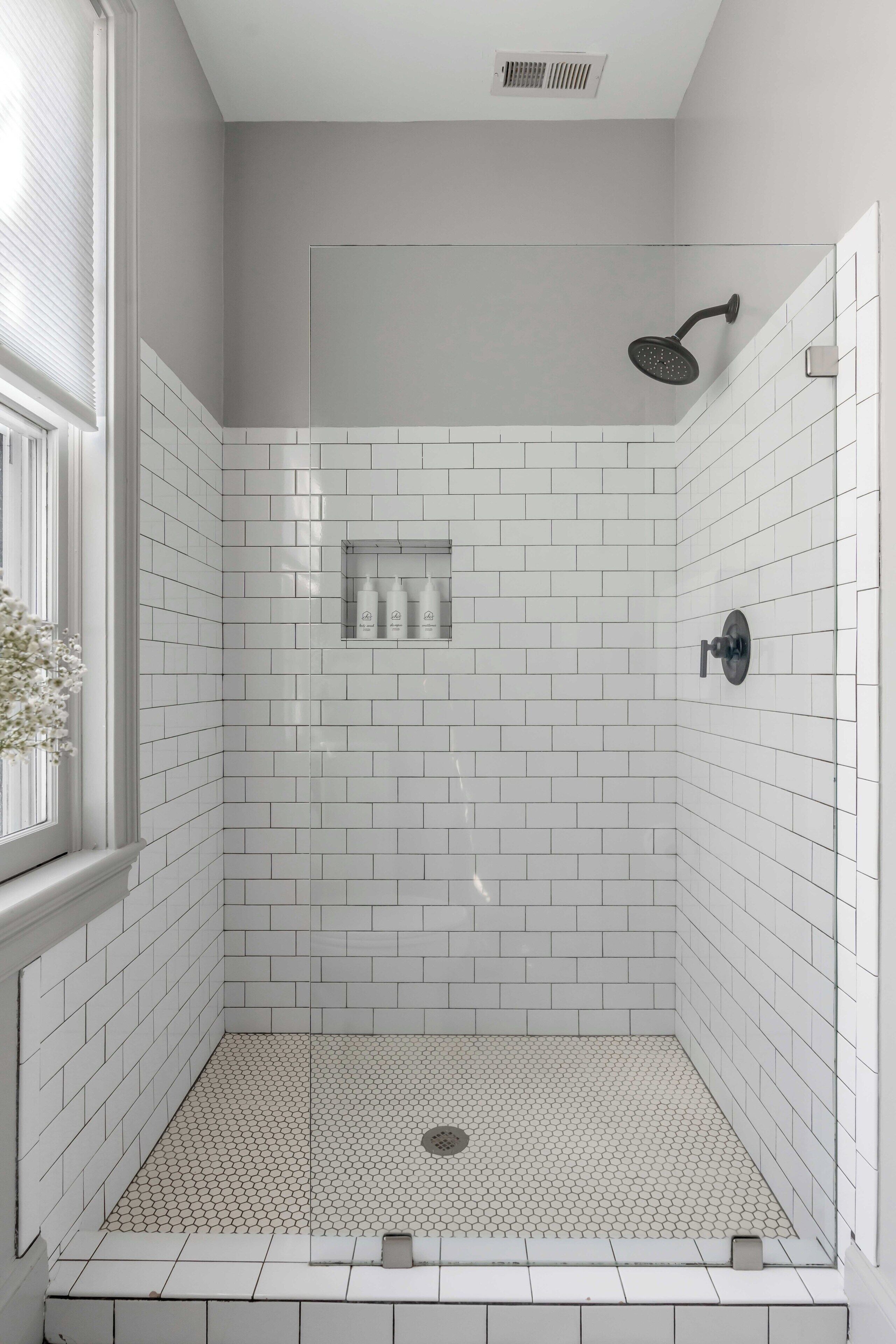 Een douche met witte tegels, een glazen deur en een douchekop.