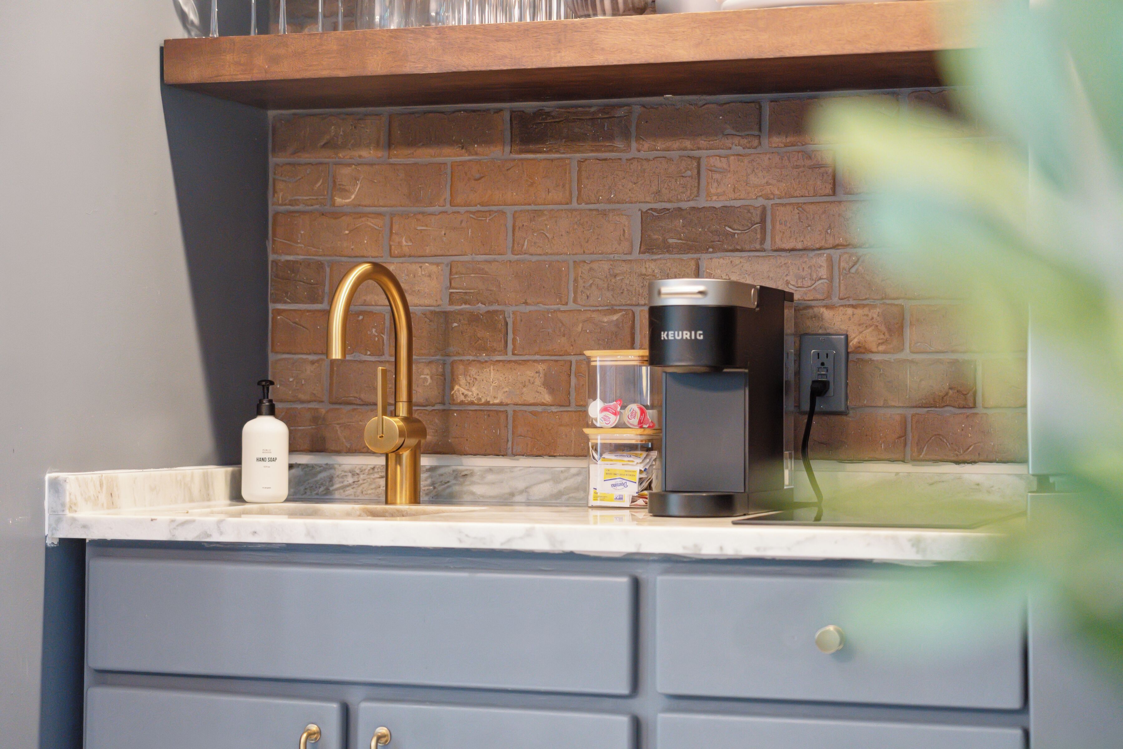 A kitchen with a marble countertop, a gold faucet, a Keurig coffee maker, and a bottle of hand soap.