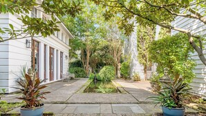 Un patio con una fuente central, rodeado de edificios blancos y diversas plantas.