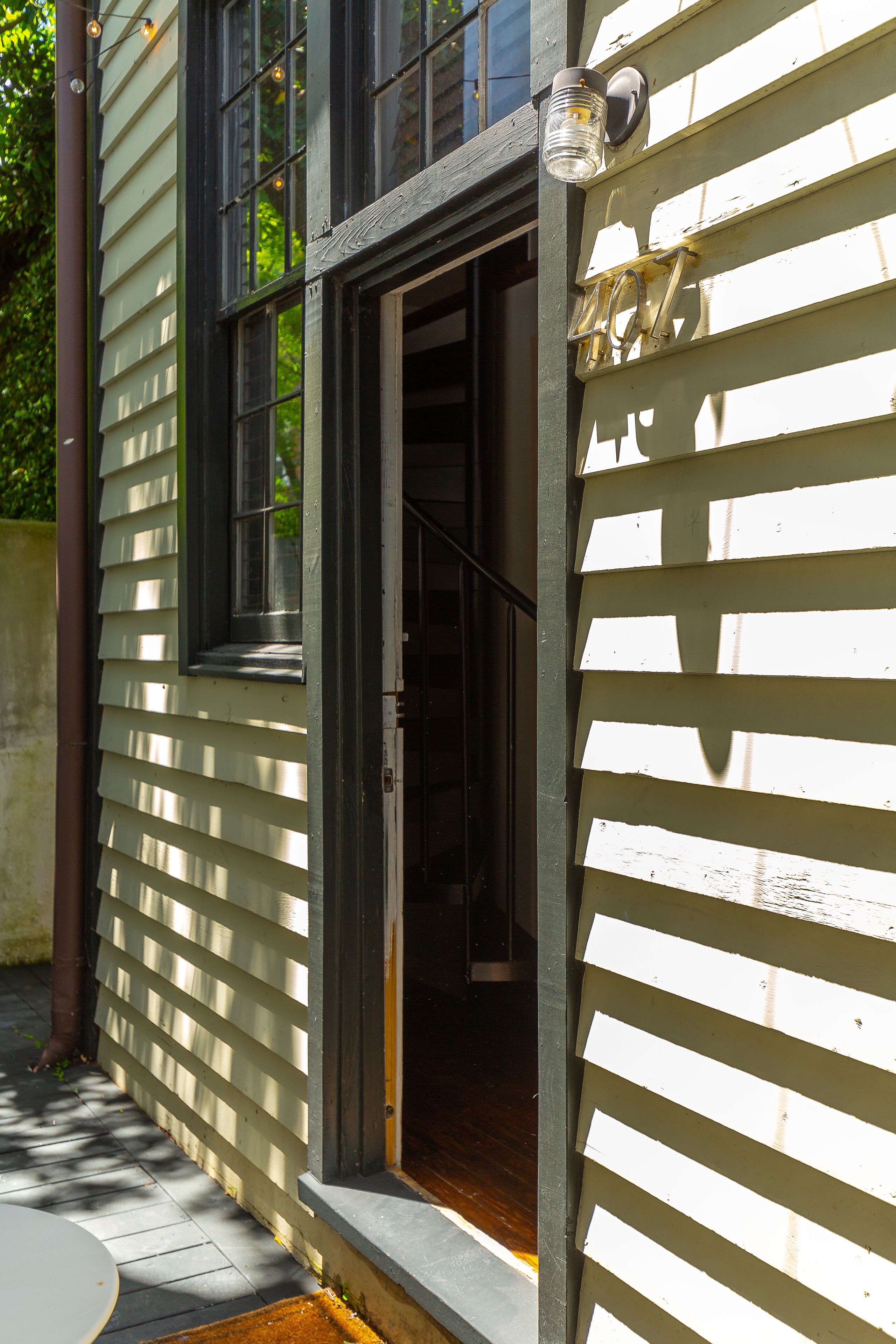 A wooden house with a visible door and window, a number '207' on the wall, and a small outdoor area with a table.