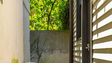 A small patio with a table and two chairs, a wooden door, and a concrete wall with some greenery.