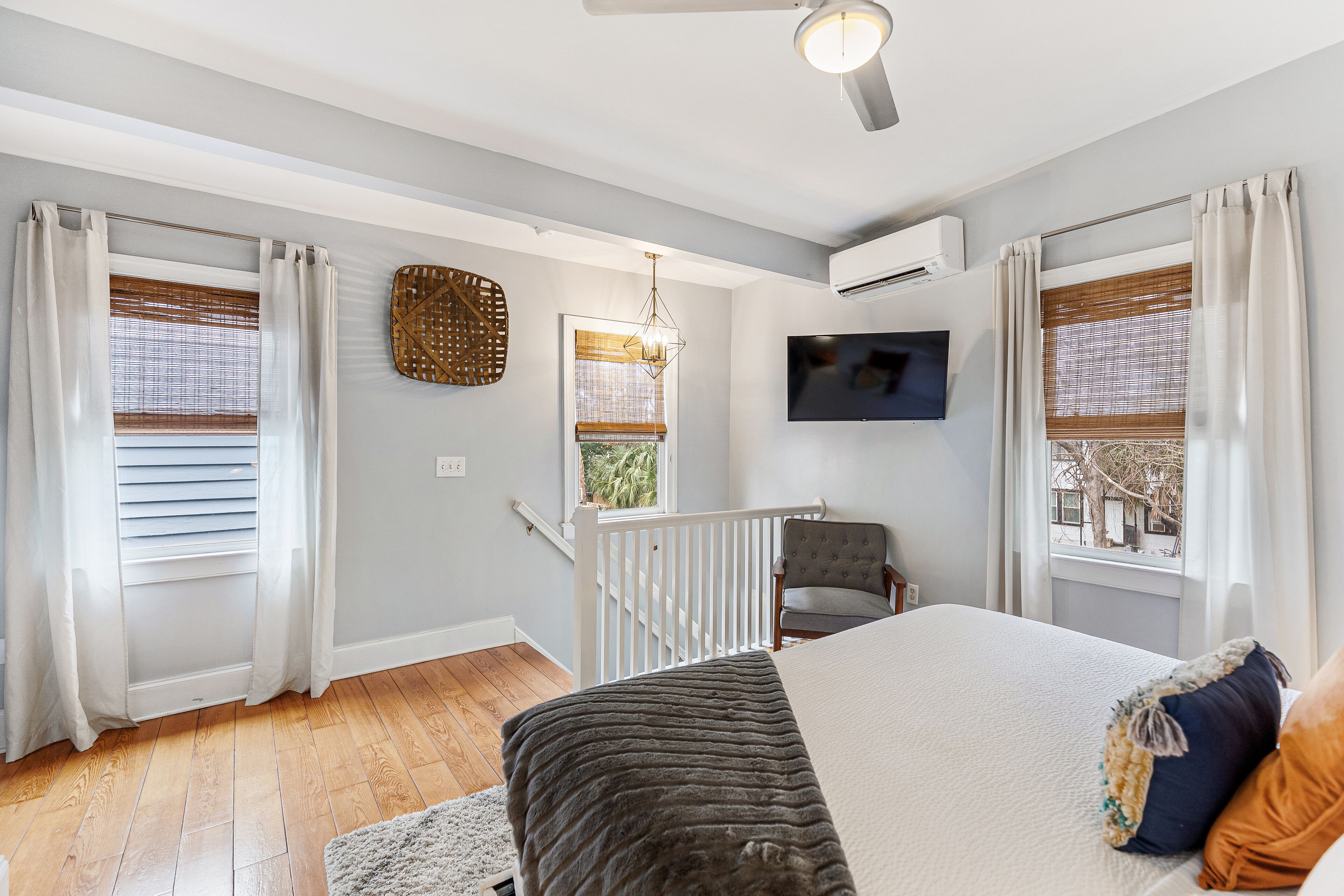 A bedroom with a bed, a chair, a TV, and a balcony with a railing.