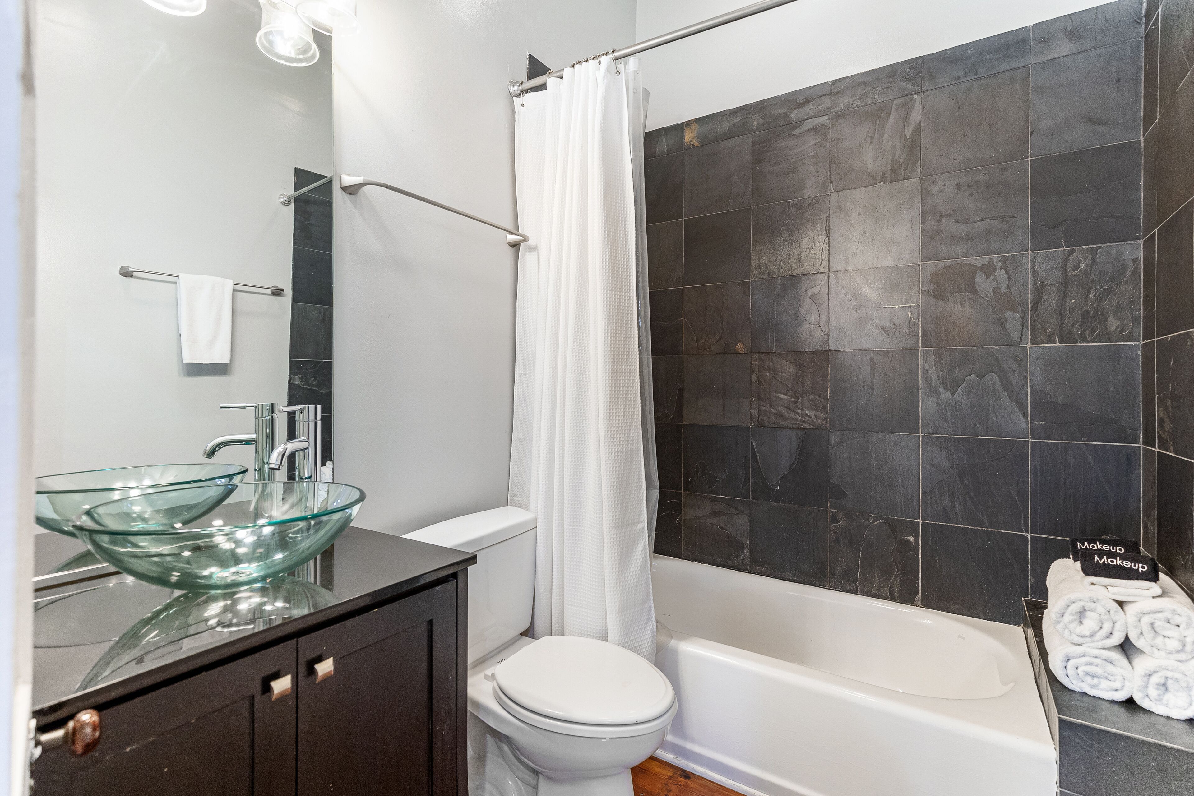 A bathroom with a glass bowl sink, a white toilet, a bathtub, and a shower curtain.