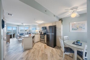 Une cuisine moderne avec des meubles blancs, un réfrigérateur noir et un coin repas comprenant une table et des chaises blanches.