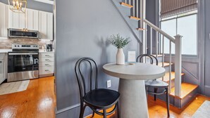 A modern kitchen with stainless steel appliances, a dining area with a round table and chairs, and a staircase with wooden steps and white railings. - Beautiful Renovated Apartment Near King Street (Charleston)