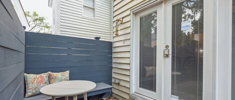 A patio with a white table and blue bench, a door with a screen, and a brick pathway.