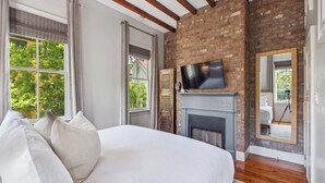 A bedroom with a large bed, a fireplace, a television, and a brick wall. - Beautiful Renovated Apartment Near King Street (Charleston)